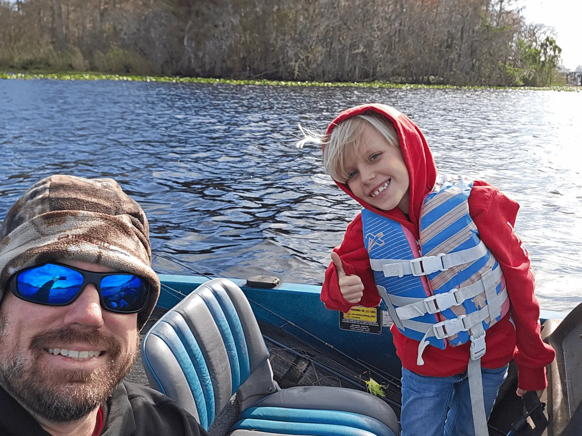 A man and a child smiling on a boat by the water.